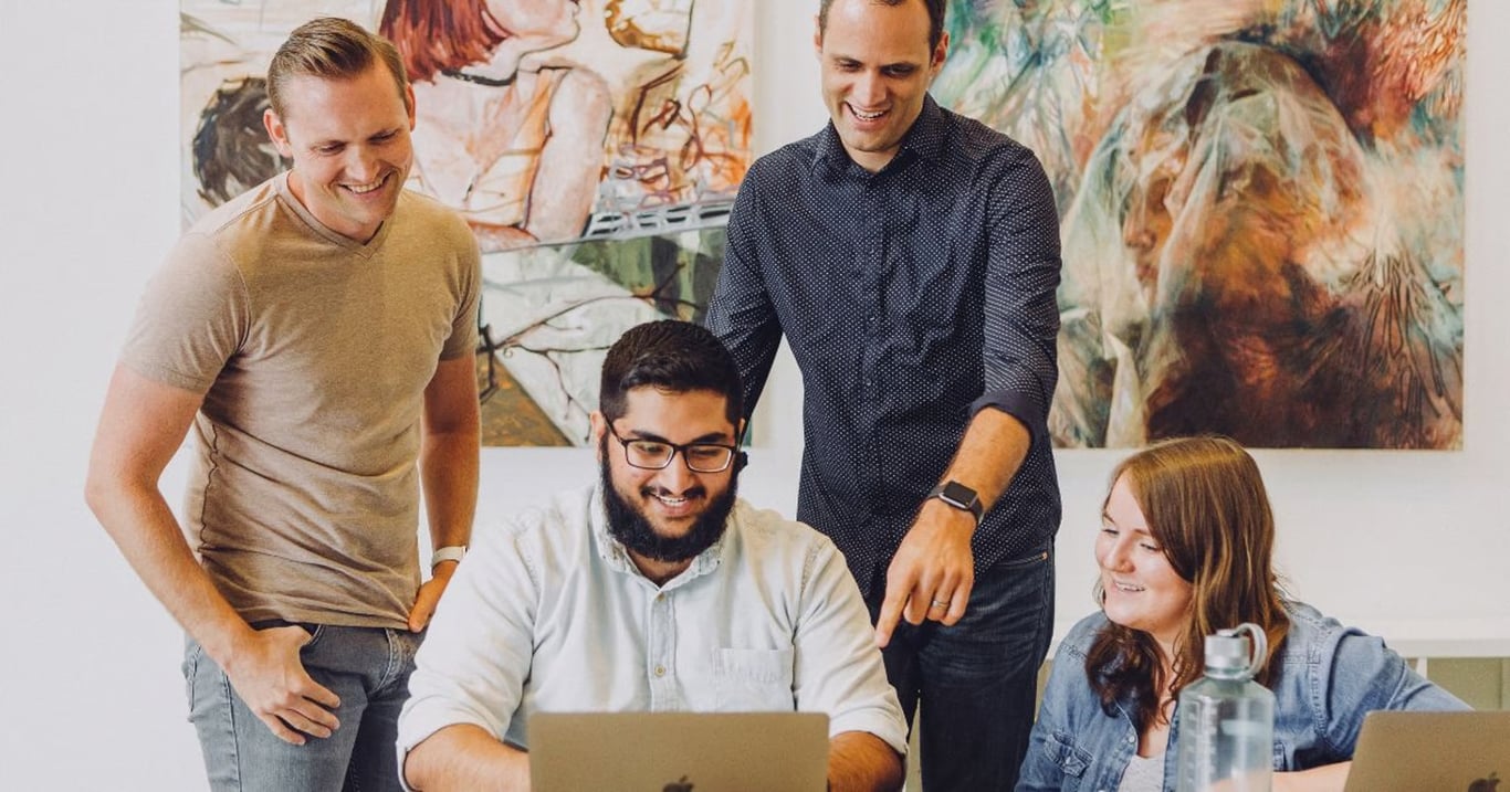 4 people looking into one laptop